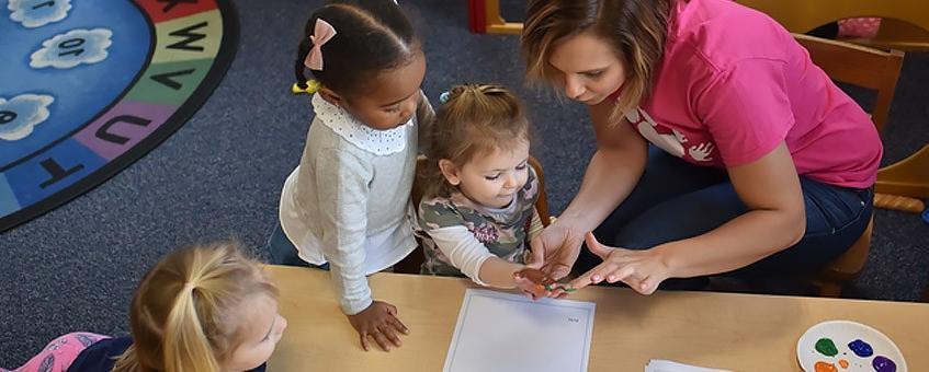 A student works with a group of children in the classroom making hand painted prints.